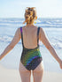 Holographic snake scale one-piece swimsuit featuring hexagon pattern with electric green, purple and blue scales on black background. Cheeky cut with scoop neck and low back design. Alternative gothic swimwear perfect for festivals, raves, beach parties. Available XS-3X, UPF 50+ protection with moisture-wicking fabric.